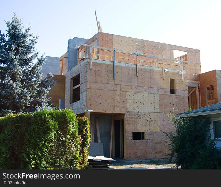 Home construction with wood framing and roof trusses and window openings and plywood and a blue sky. Home construction with wood framing and roof trusses and window openings and plywood and a blue sky.