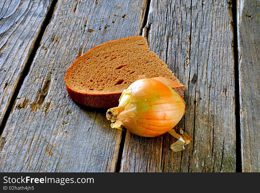 A piece of black bread and a slice of onion on an old wooden table. A piece of black bread and a slice of onion on an old wooden table