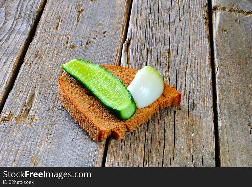 A slice of black bread, onion and cucumber on an old wooden table. A slice of black bread, onion and cucumber on an old wooden table