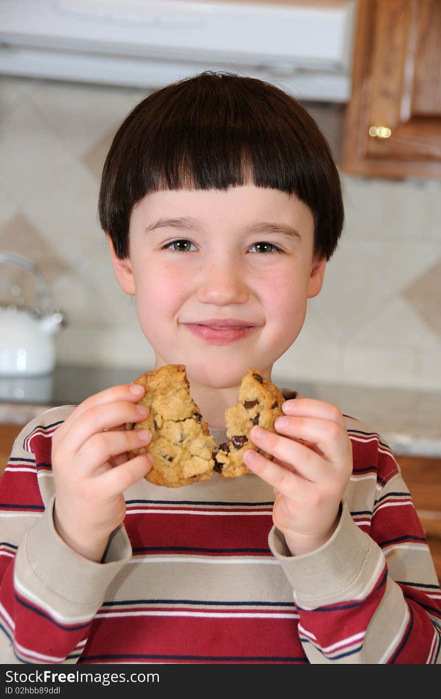 A little boy smiles as he breaks a chocolate chip cookie before eating it. A little boy smiles as he breaks a chocolate chip cookie before eating it