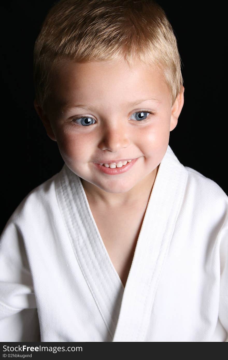 Young boy wearing his karate uniform on a black background. Young boy wearing his karate uniform on a black background