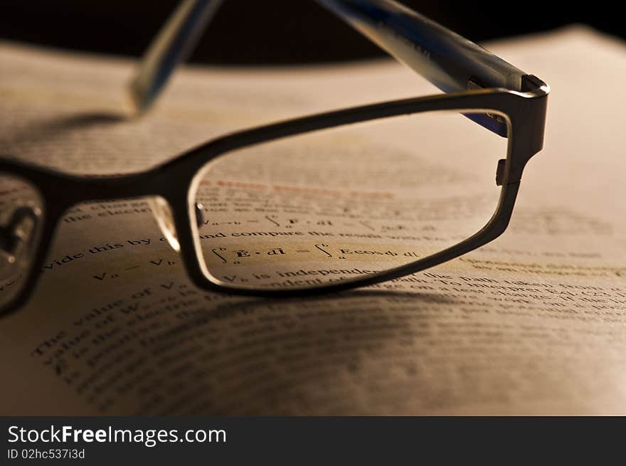 A book (University physics) and a pair of glasses. Focus on an equation, through the glasses. A book (University physics) and a pair of glasses. Focus on an equation, through the glasses.