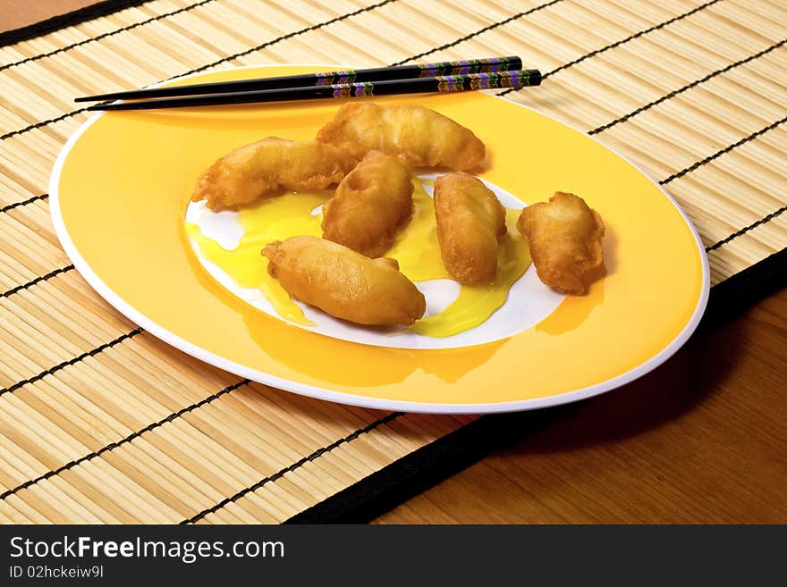 Yellow plate with chicken, lemon sauce and chopsticks on bamboo placemat.  Horizontal. Yellow plate with chicken, lemon sauce and chopsticks on bamboo placemat.  Horizontal.