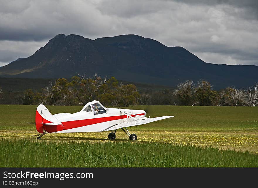 White and red glider tow plane spotlighted by sun in bright green wheat field, with a contrasting moody back drop of a mountain and foreboding sky. White and red glider tow plane spotlighted by sun in bright green wheat field, with a contrasting moody back drop of a mountain and foreboding sky.