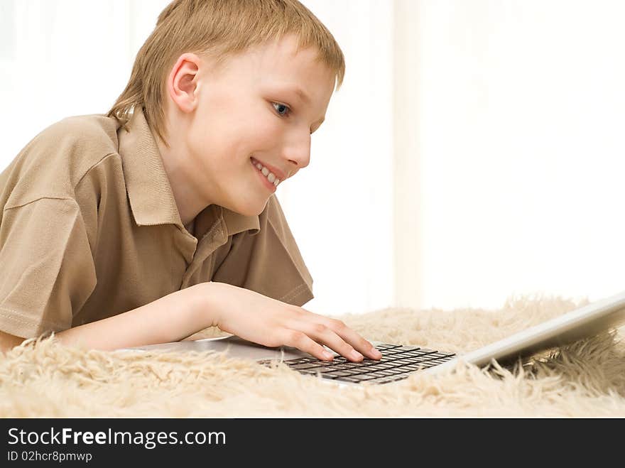 Happy young boy lies and playing on a laptop. Happy young boy lies and playing on a laptop