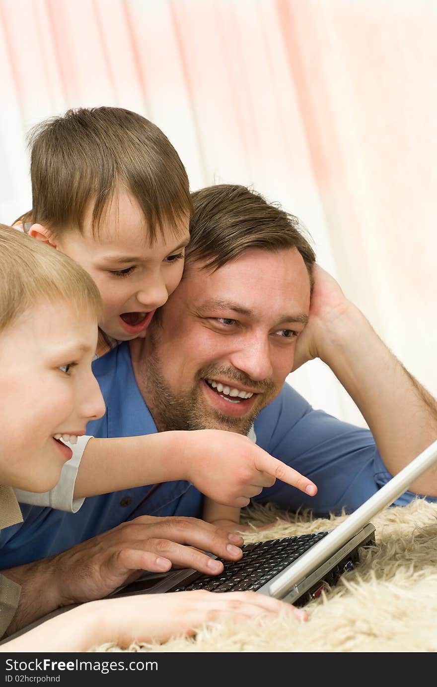 Young father with his sons is on the carpet with laptop