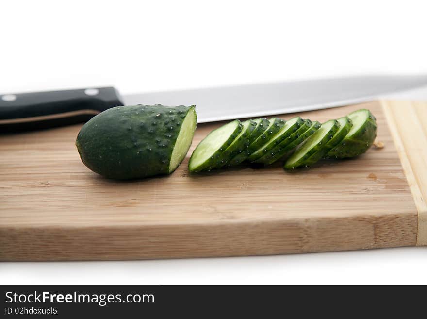 The green cucumber cut on segments and a knife on a bamboo board. The green cucumber cut on segments and a knife on a bamboo board