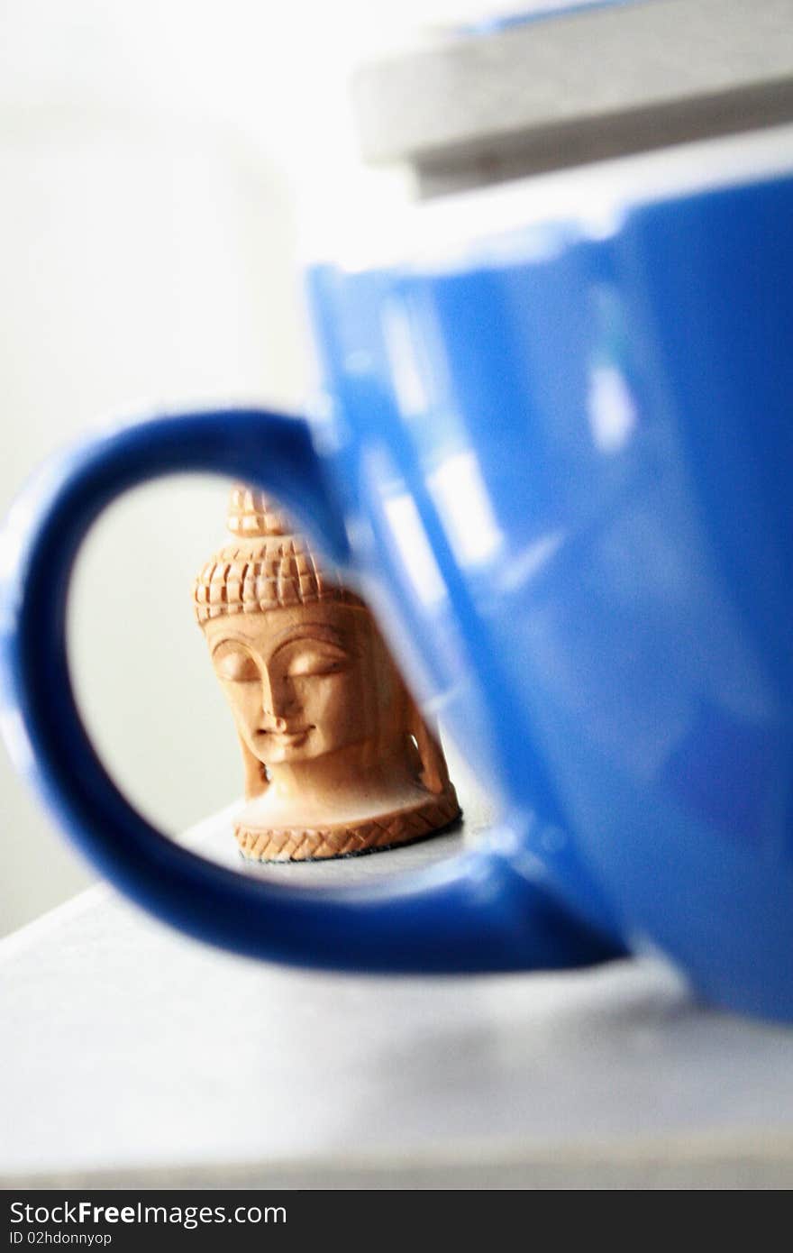 A Buddha head looks through a blue coffee mug. A Buddha head looks through a blue coffee mug