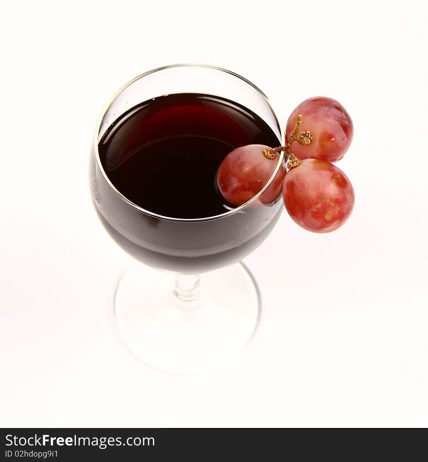 Red wine in a wineglass with three red grapes on white background