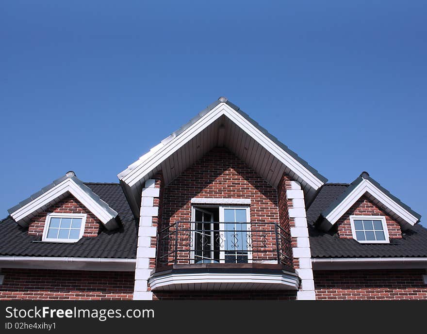 Top of house with windows and balcony against blue sky. Top of house with windows and balcony against blue sky