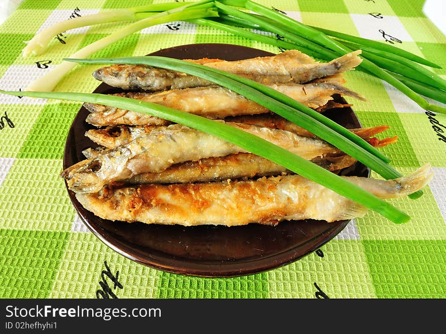 Image of fried fish capelin in the saucer with green onions. Image of fried fish capelin in the saucer with green onions