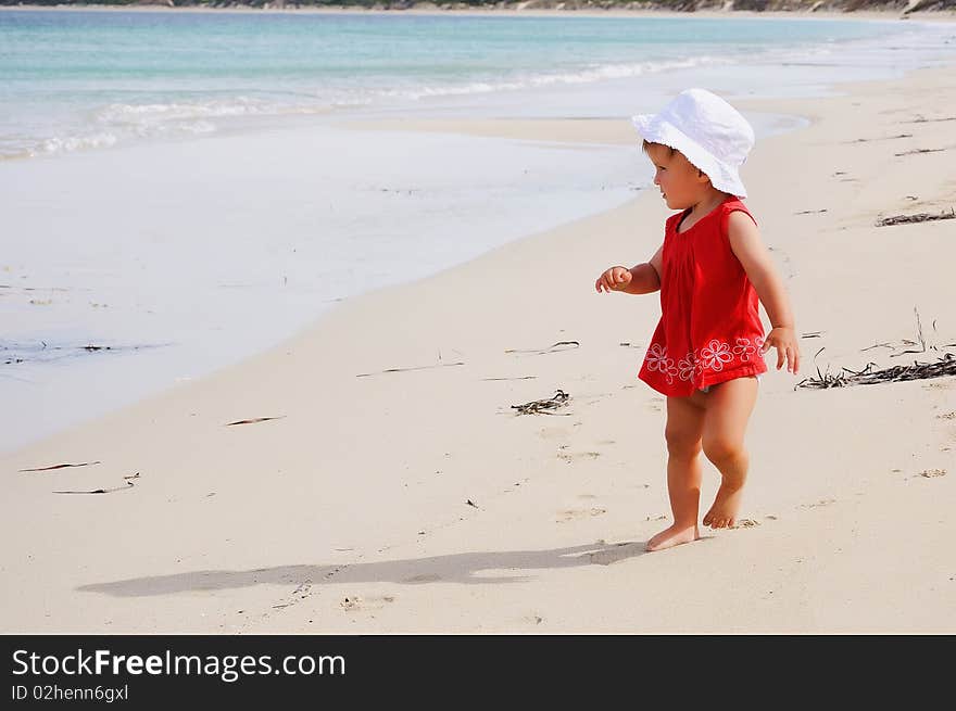 Little happy girl in a red dress and a white Panama hat on the beach