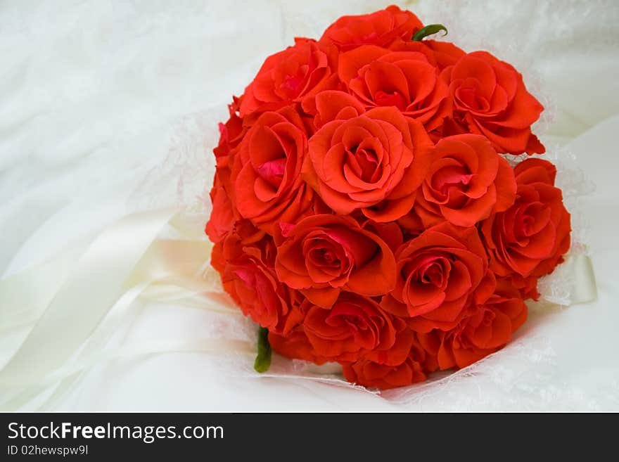 The round bouquet of red roses on white silk is decorated by satiny tapes