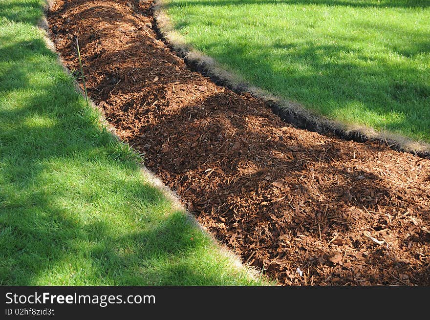 Pathway of brown bark wood going across a green grass yard lawn