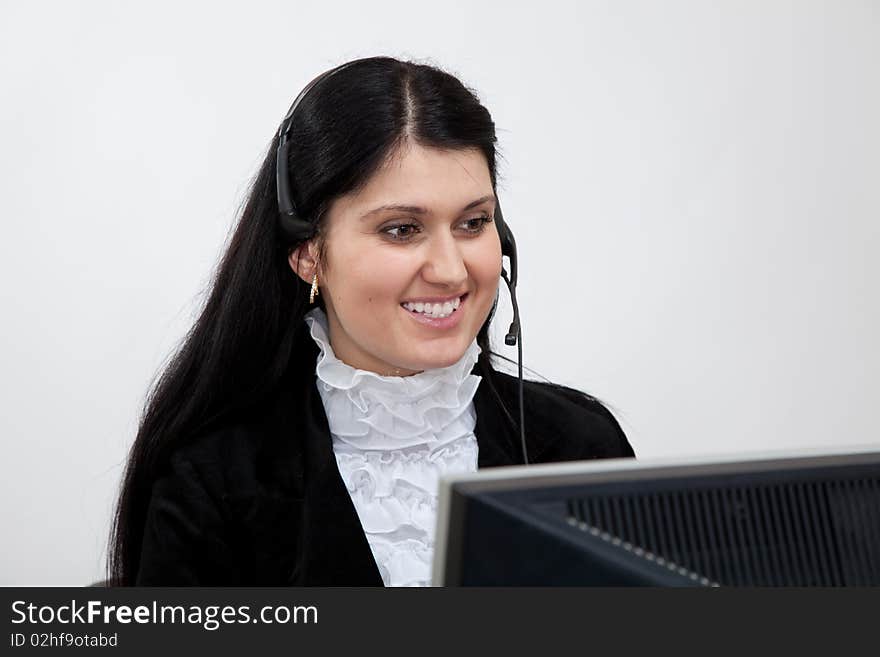 Young smiling brunette woman with headphones sits at a table in front of the monitor. Young smiling brunette woman with headphones sits at a table in front of the monitor.