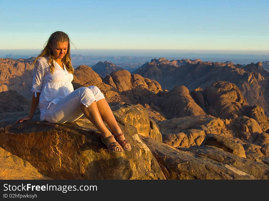 A girl sitting on a mountaintop in the setting sun. A girl sitting on a mountaintop in the setting sun