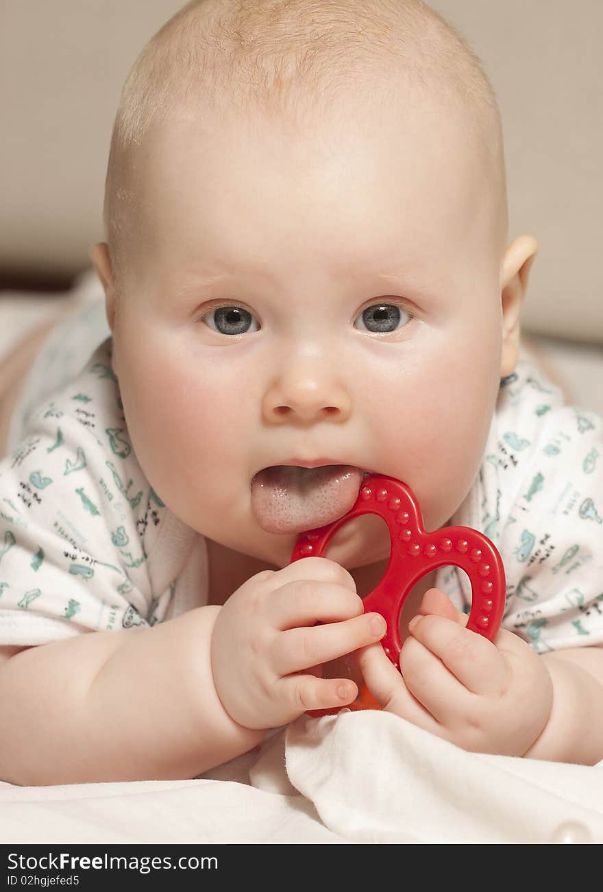 Portrait of a baby girl (9 months) at home. Baby licking a plastic toy