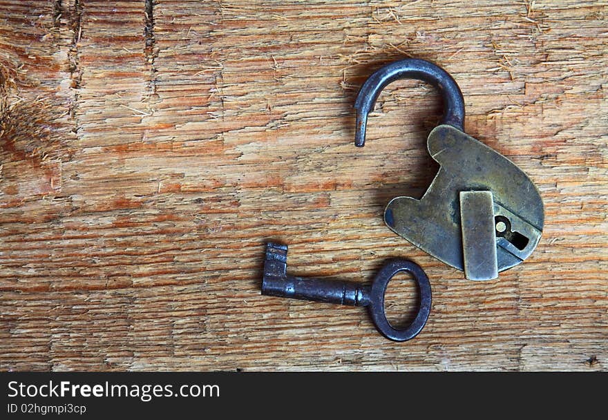 Old padlock and key on wooden background