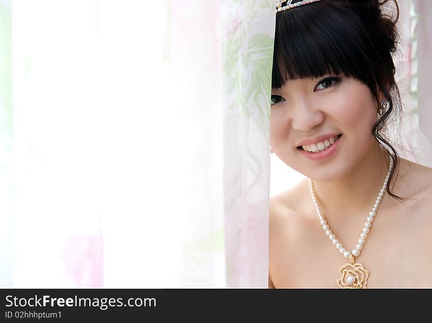 A beautiful chinese  bride at the window. She is dressed  a beautiful necklace. A beautiful chinese  bride at the window. She is dressed  a beautiful necklace