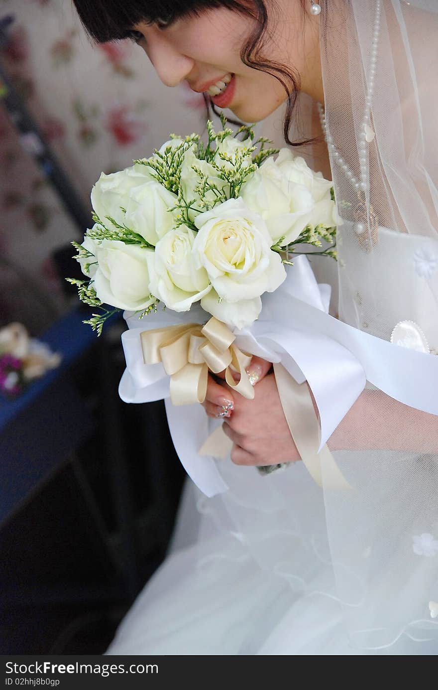 A beautiful chinese  bride looks down at her bouquet. She is dressed in a simple gown and wearing a tiara. A beautiful chinese  bride looks down at her bouquet. She is dressed in a simple gown and wearing a tiara.