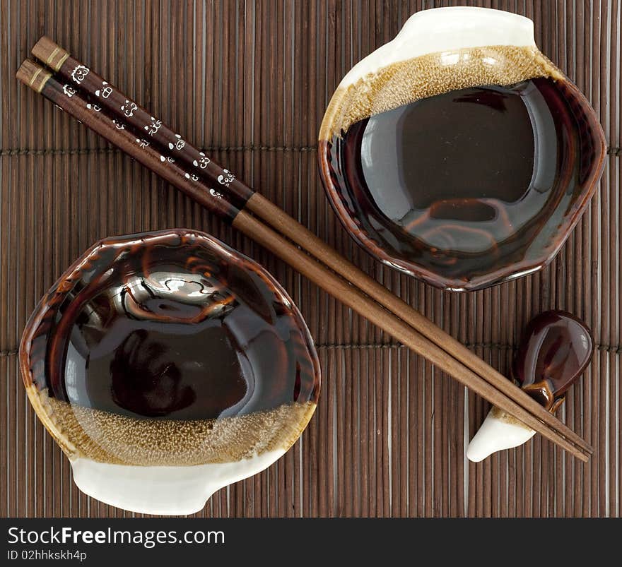 Sticks fo sushi and two porcelain plates on the brown bamboo mat. Sticks fo sushi and two porcelain plates on the brown bamboo mat