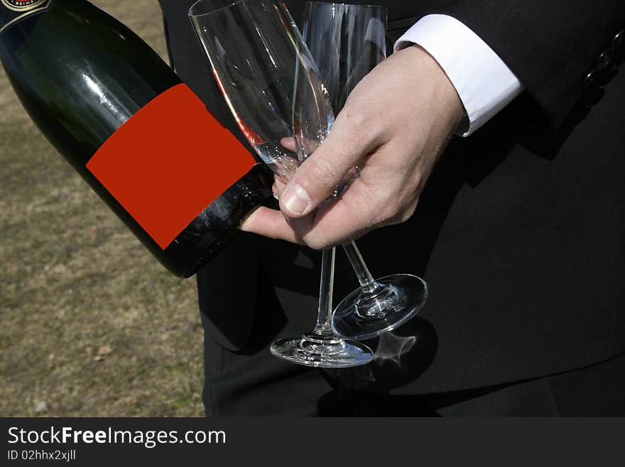 A man in suit holding two wine glasses and bottle of wine with a red label, good for copyspace. A man in suit holding two wine glasses and bottle of wine with a red label, good for copyspace