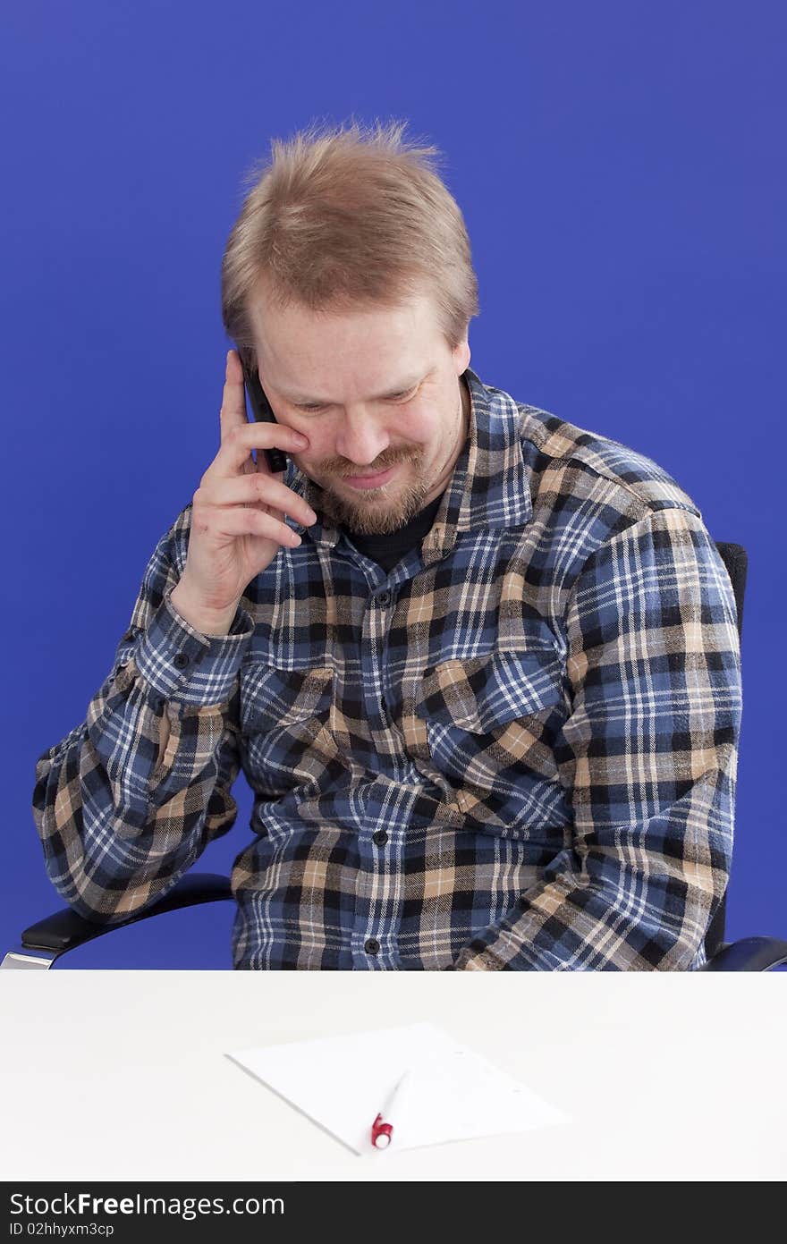 Casually dressed manager (male) takes a personal phone call at his office desk while looking down. Casually dressed manager (male) takes a personal phone call at his office desk while looking down.