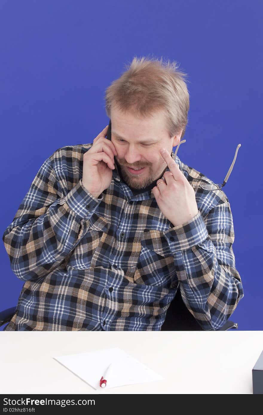 Casually dressed manager (male) takes a personal phone call at his office desk while looking down. Casually dressed manager (male) takes a personal phone call at his office desk while looking down.