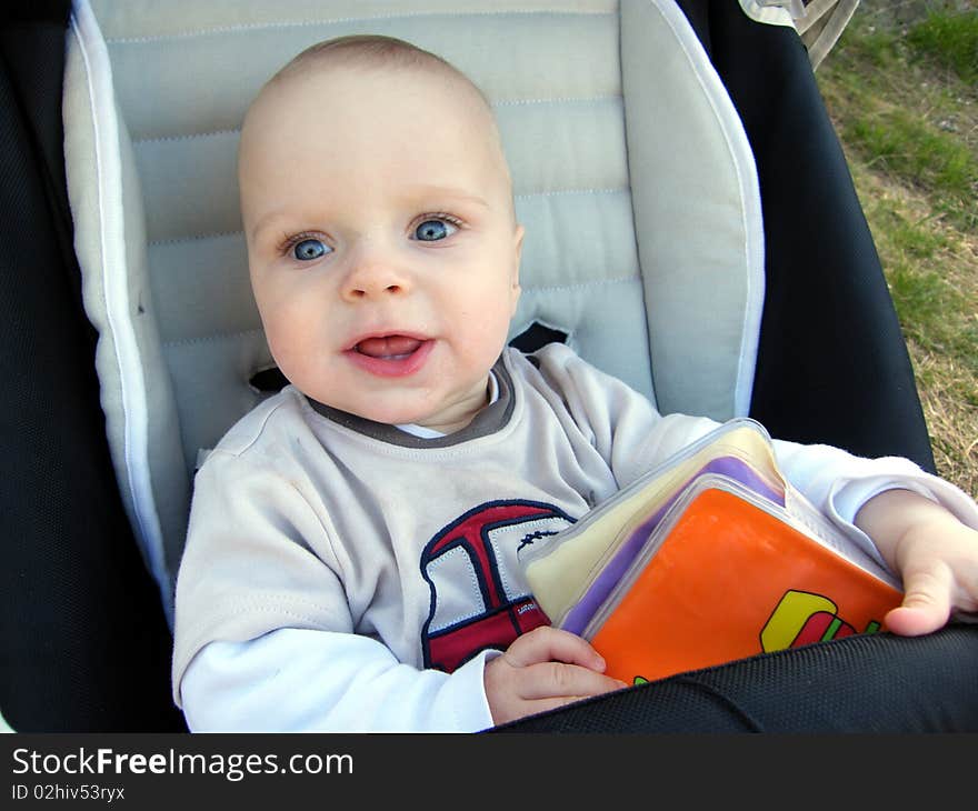 7 month old curious baby boy in pram with a book