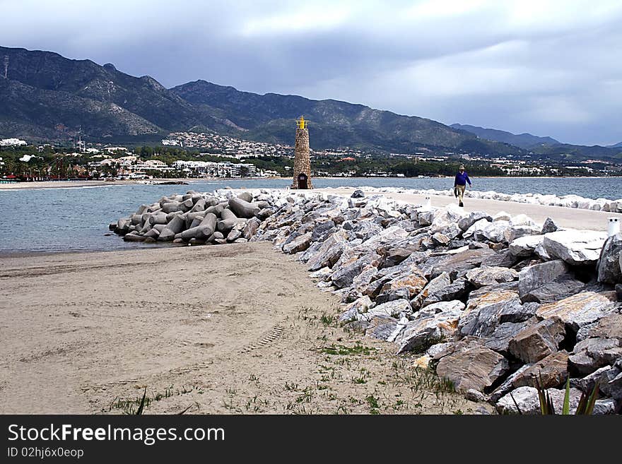 Lighthouse at end of jetty on the beach, with mountains and sky in the background. Lighthouse at end of jetty on the beach, with mountains and sky in the background.