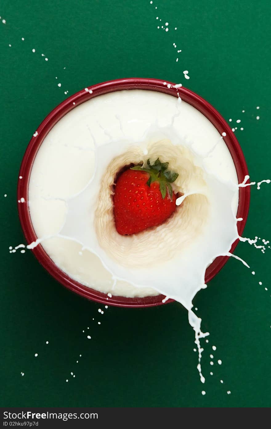 Strawberry dropped into bowl of milk, creating a splash sculpture. Strawberry dropped into bowl of milk, creating a splash sculpture