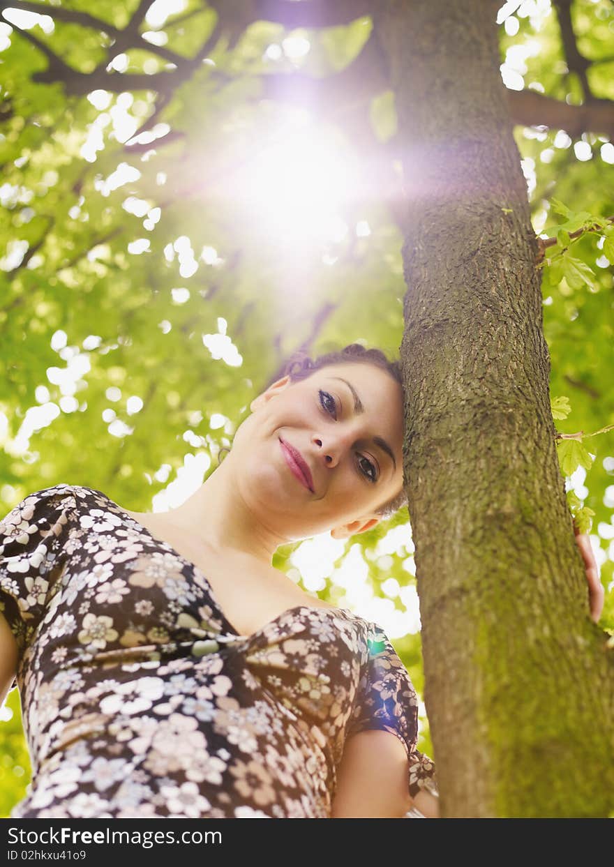 Potrait of attractive caucasian woman leaning on tree at sunset and looking away. Low angle view, vertical shape. Potrait of attractive caucasian woman leaning on tree at sunset and looking away. Low angle view, vertical shape