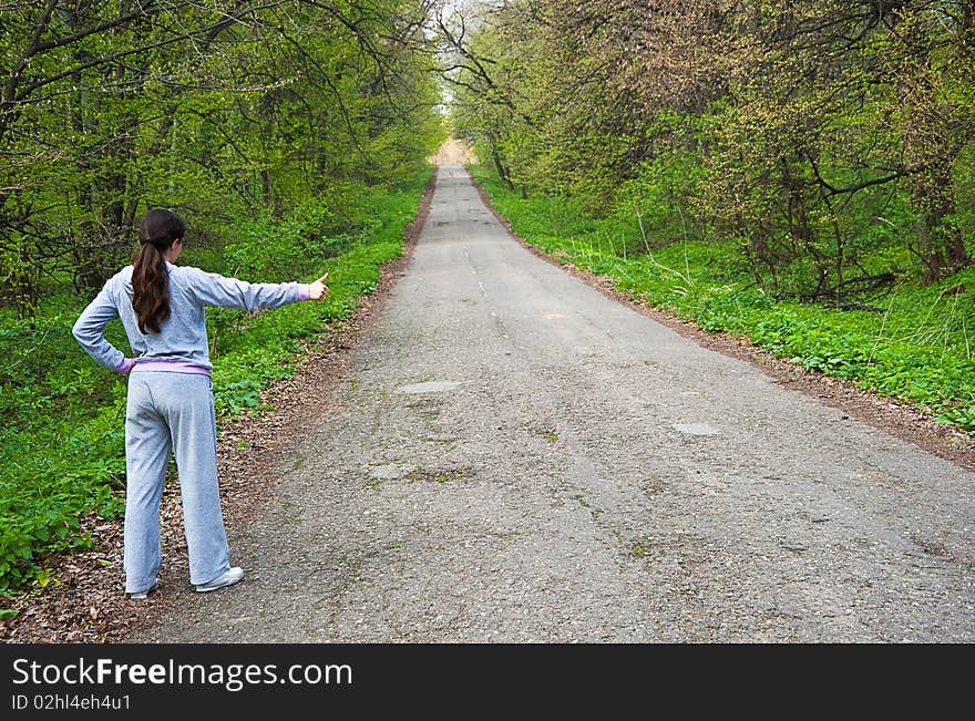 Girl hitch hiking near a road in the forest