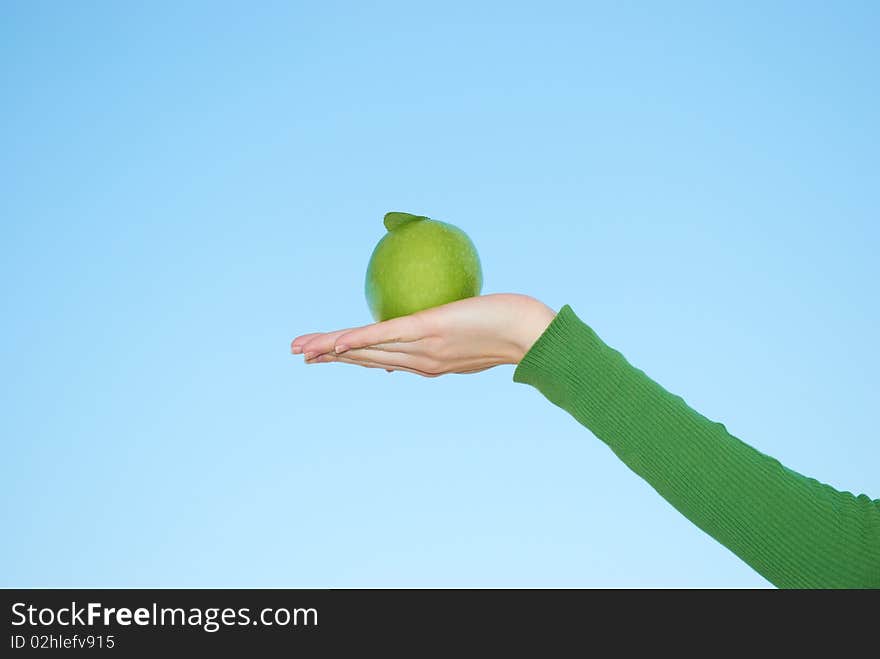 Green apple in a hand on a background of the sky