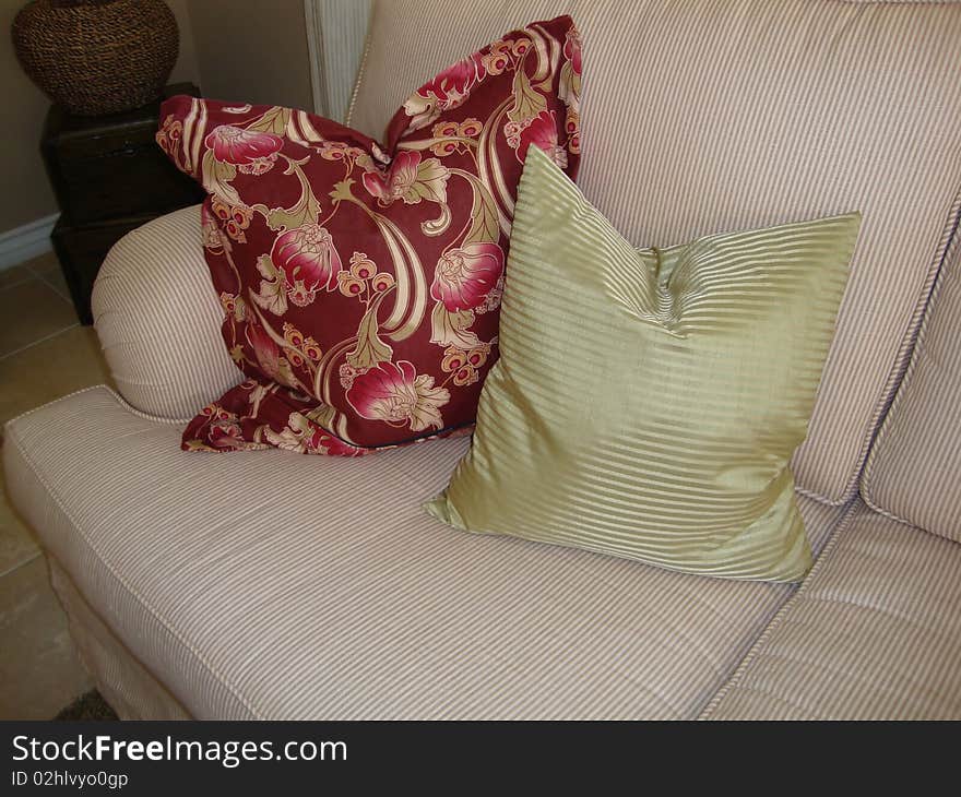 Two beautiful pillows on a couch or sofa one pillow is green stripes and one pillow is a print of flowers with red and pink colors. Two beautiful pillows on a couch or sofa one pillow is green stripes and one pillow is a print of flowers with red and pink colors