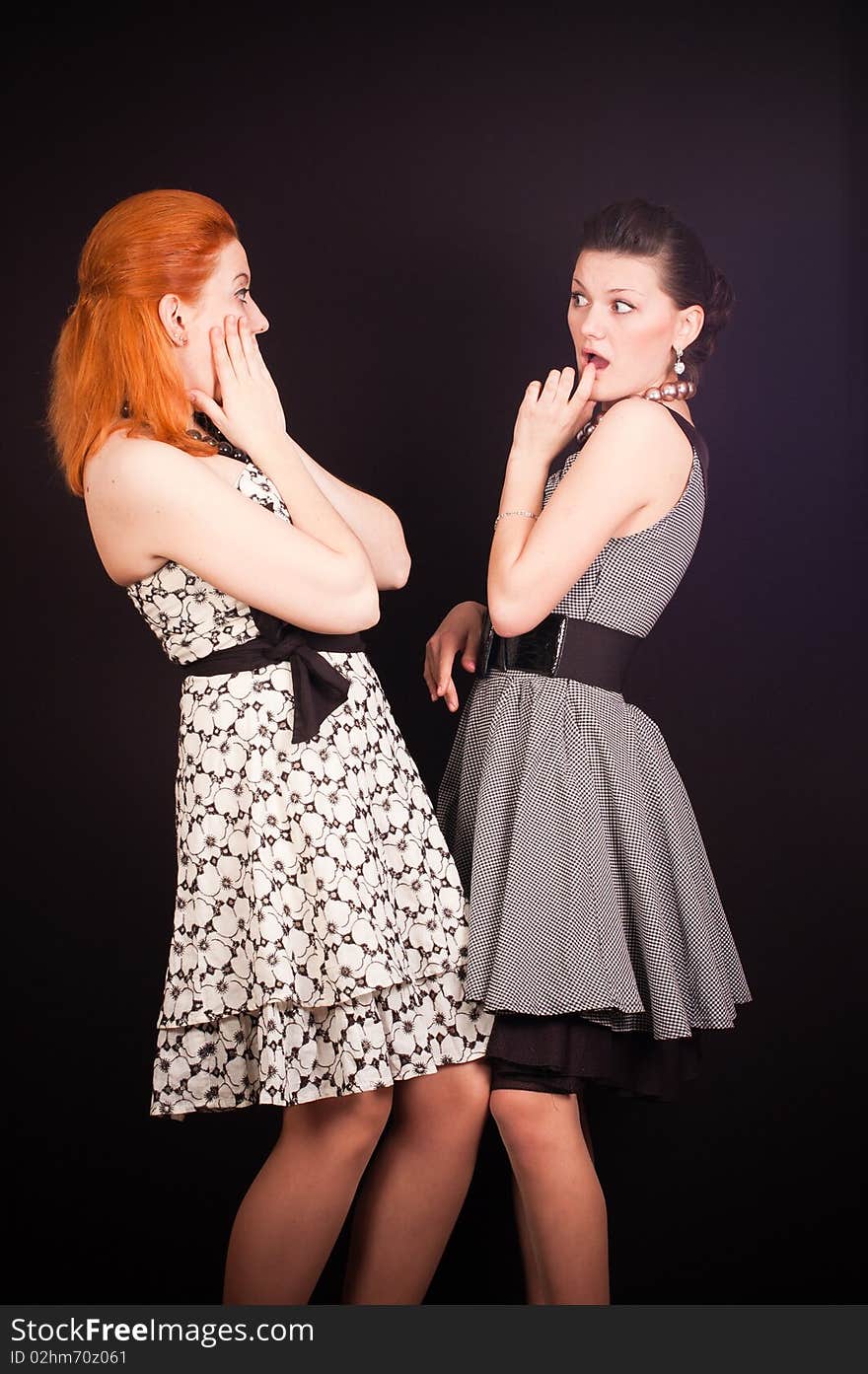 Two girls in dresses in retro style on a black background in studio