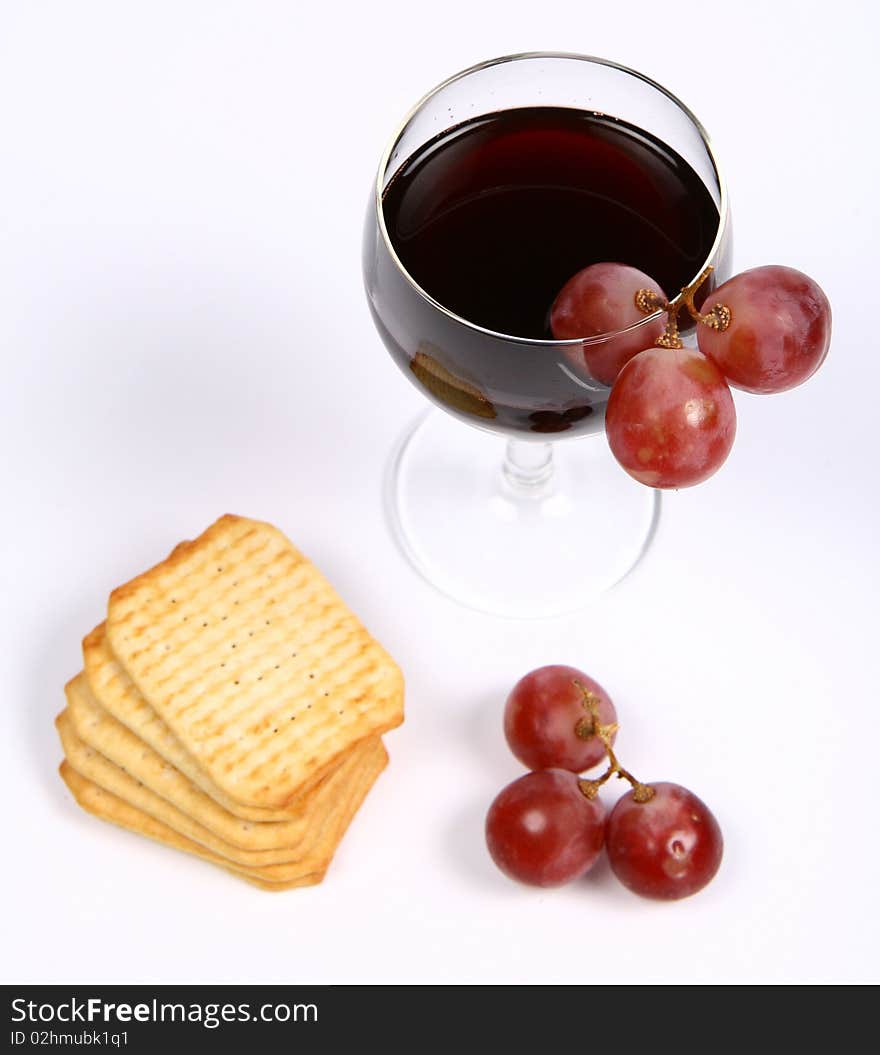 Red wine in a wineglass with red grapes and some crackers on white background