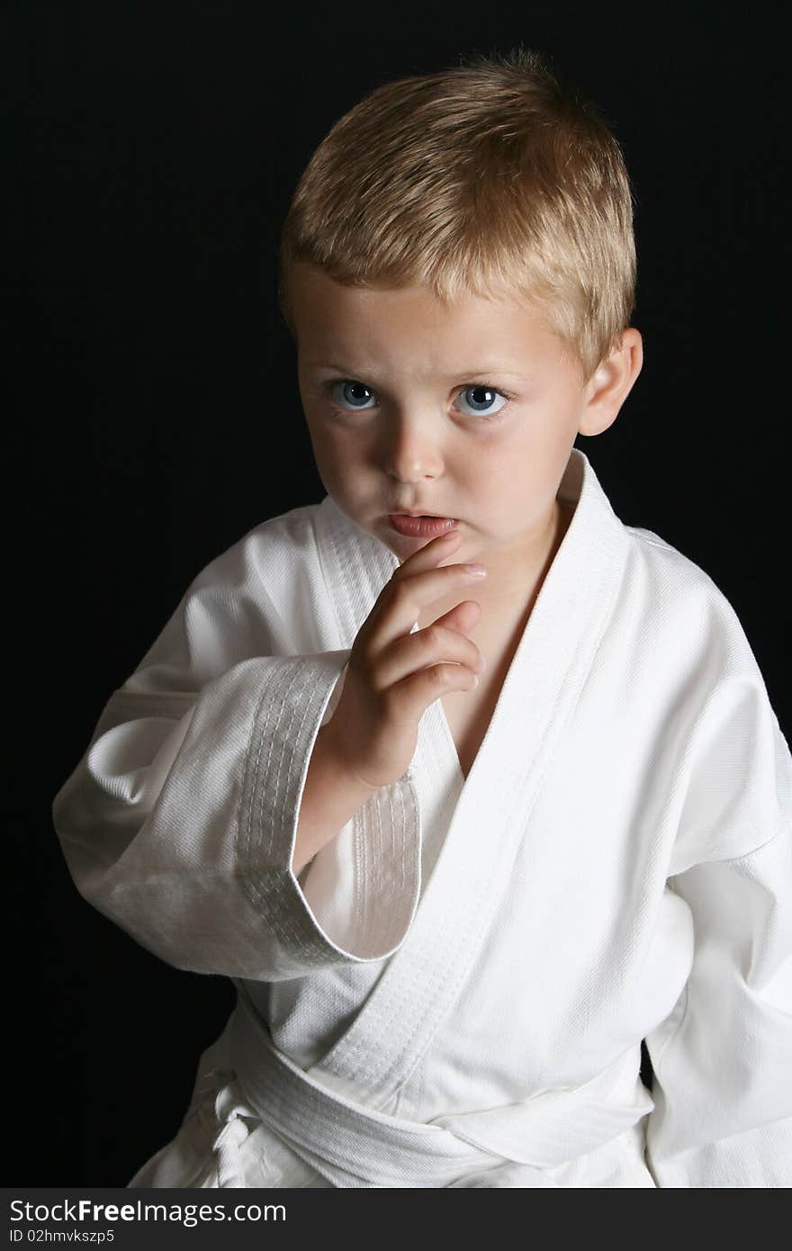 Young boy wearing his karate uniform on a black background. Young boy wearing his karate uniform on a black background