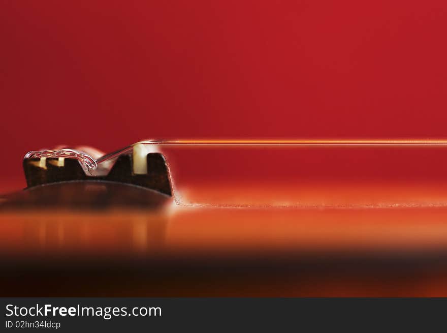 Guitar bridge and nylon strings on an out-of-focus red background. Guitar bridge and nylon strings on an out-of-focus red background.