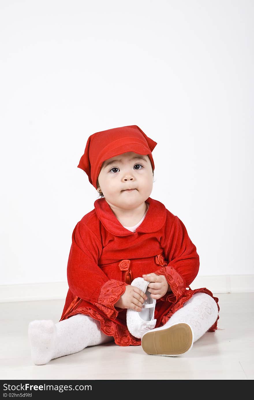 Little girl 11 months old sitting on floor dressed in little red riding hood costume and holding a shoe in her hands.Check also Children