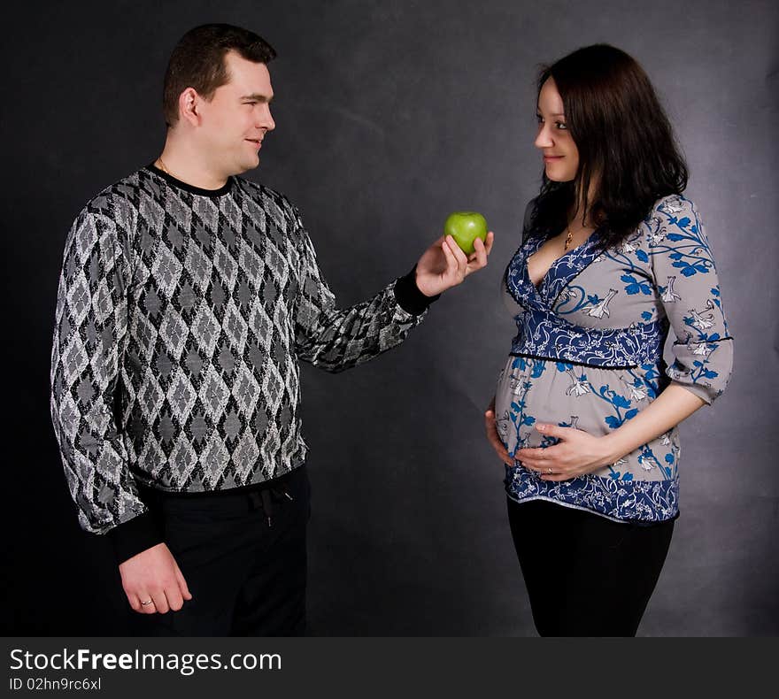 Careful man gives green apple pregnant woman on a black background. Careful man gives green apple pregnant woman on a black background