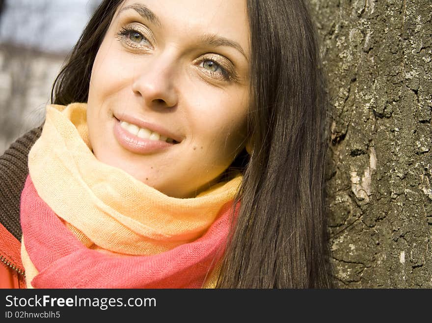 Beautiful female in a red jacket in the park based on the tree. He smiles and looks into the distance. Beautiful female in a red jacket in the park based on the tree. He smiles and looks into the distance