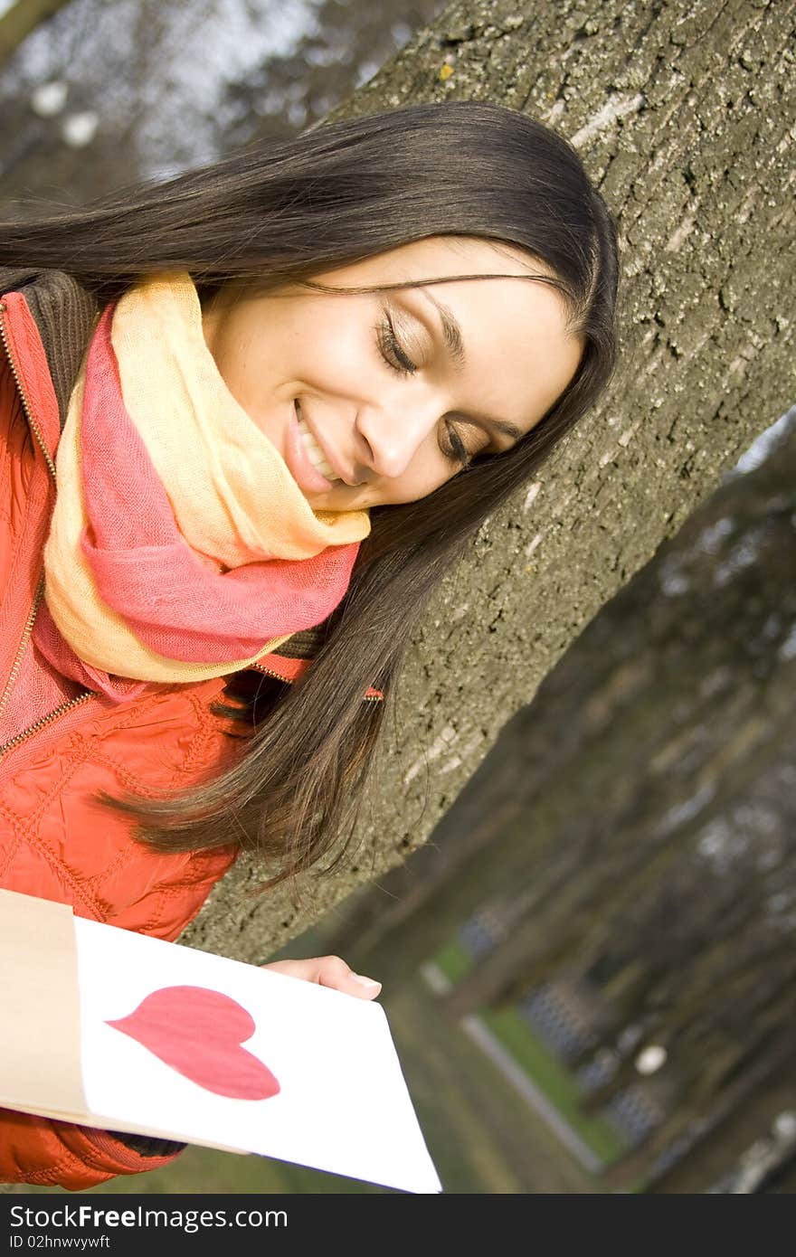 Beautiful female in the park. In the hands of an envelope with a letter. The letter pasted red heart. Beautiful female in the park. In the hands of an envelope with a letter. The letter pasted red heart