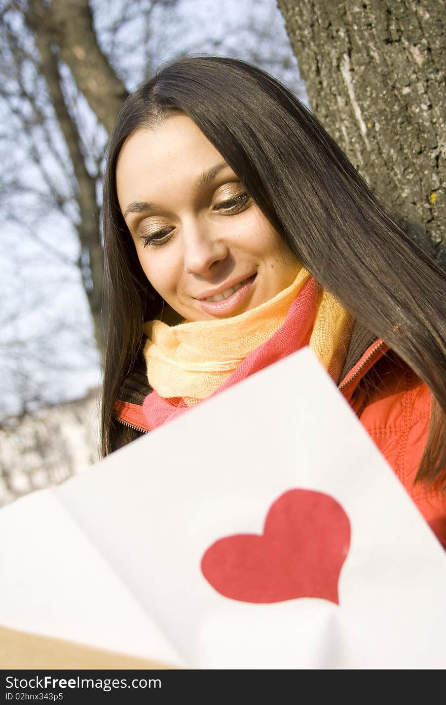 Beautiful female in the park. In the hands of an envelope with a letter. The letter pasted red heart. Beautiful female in the park. In the hands of an envelope with a letter. The letter pasted red heart