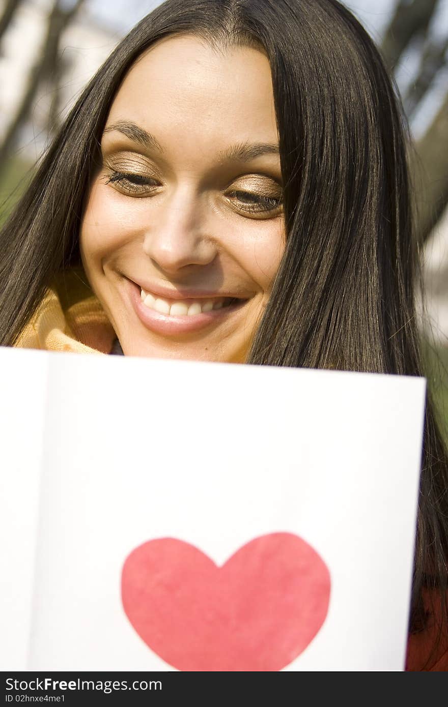 Beautiful female in the park. In the hands of an envelope with a letter. The letter pasted red heart. Beautiful female in the park. In the hands of an envelope with a letter. The letter pasted red heart