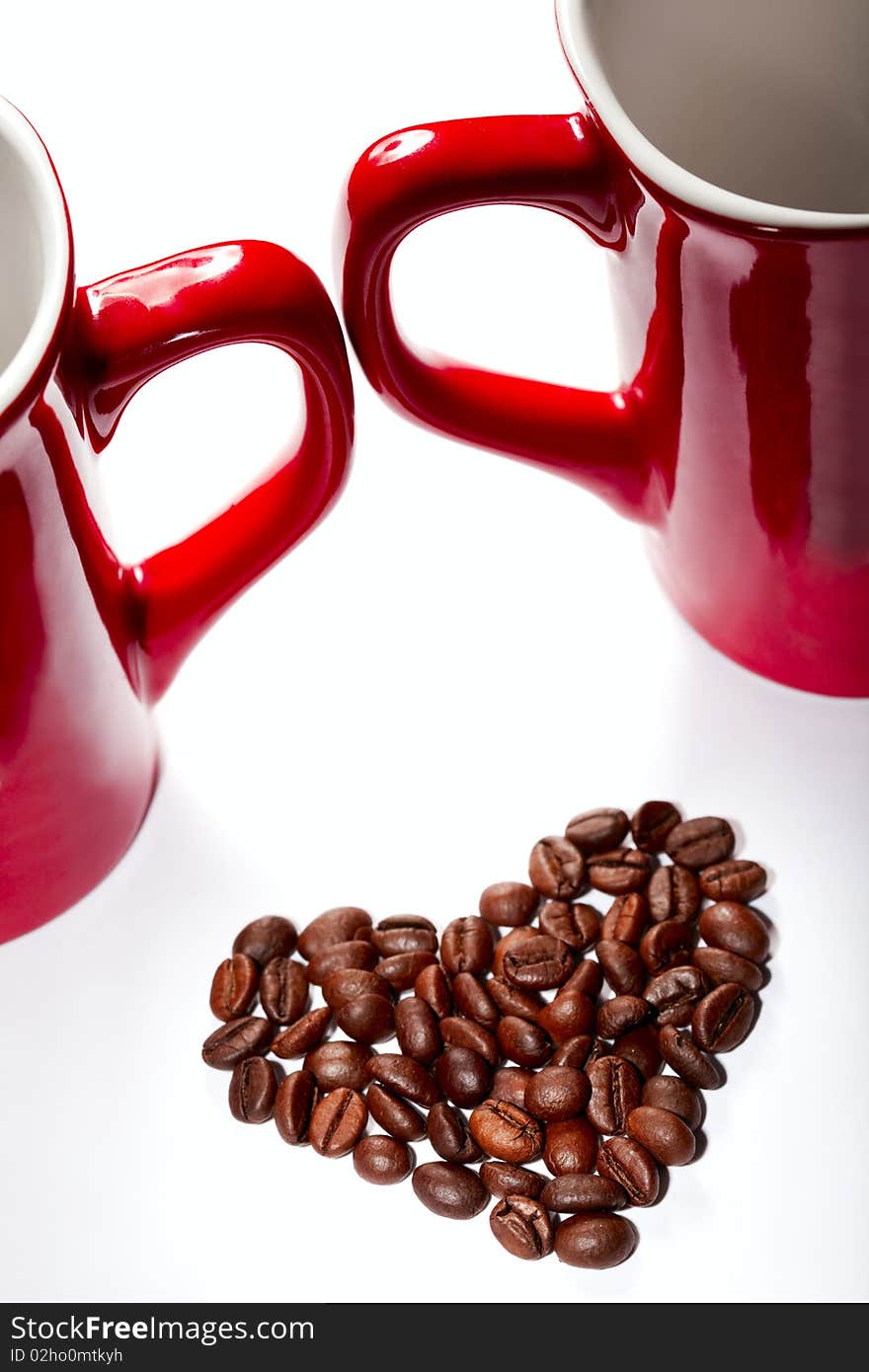 Coffee-beans heart against red cup`s handles on white backround