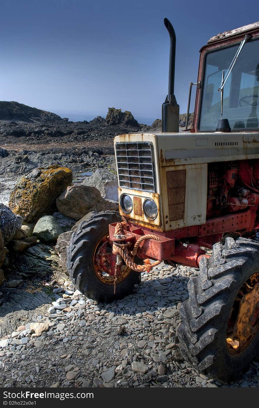 Frontside of old, rusty tractor on a pebble beach