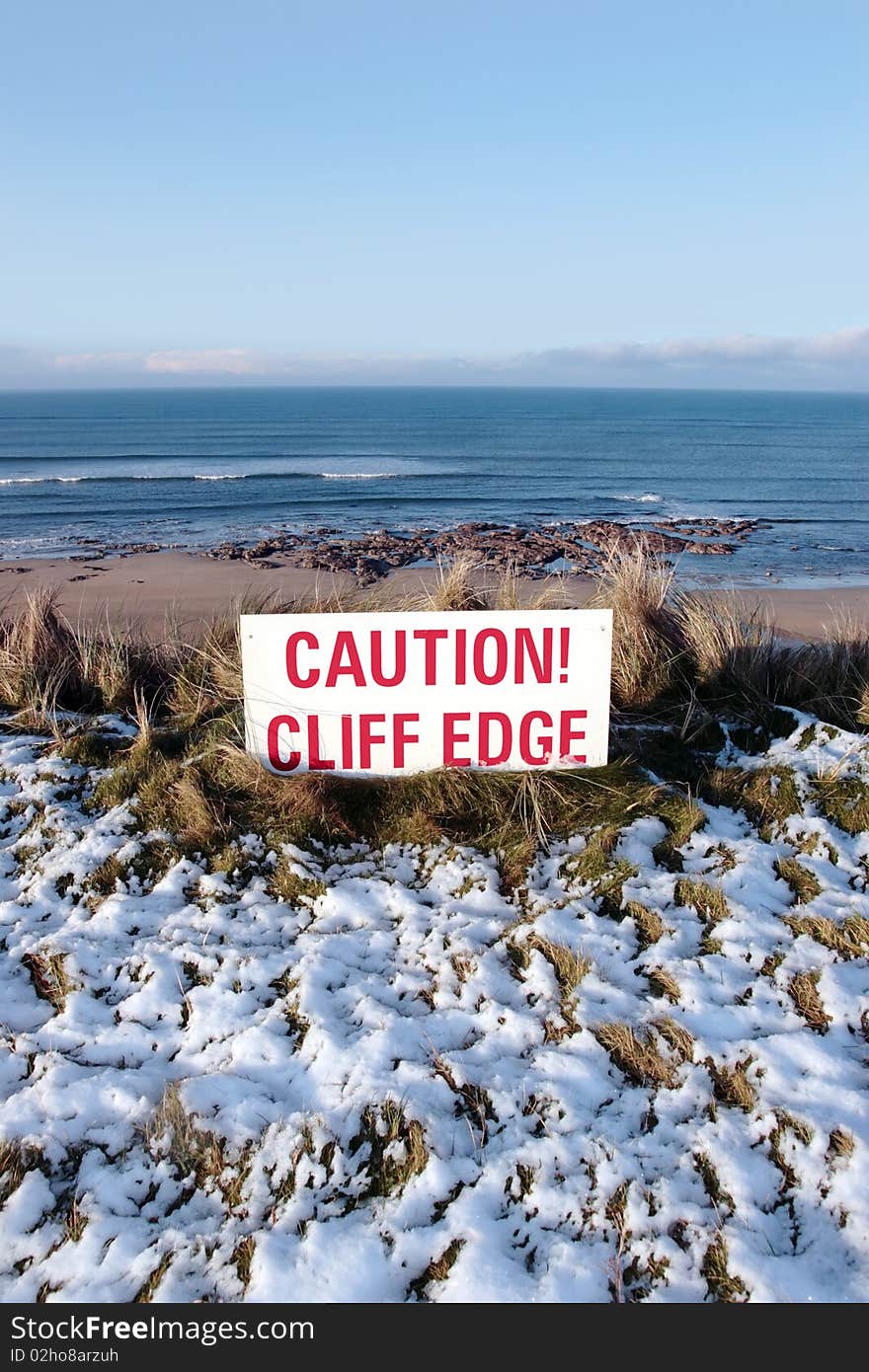 A red caution sign on a cliff edge in snow covered ballybunion