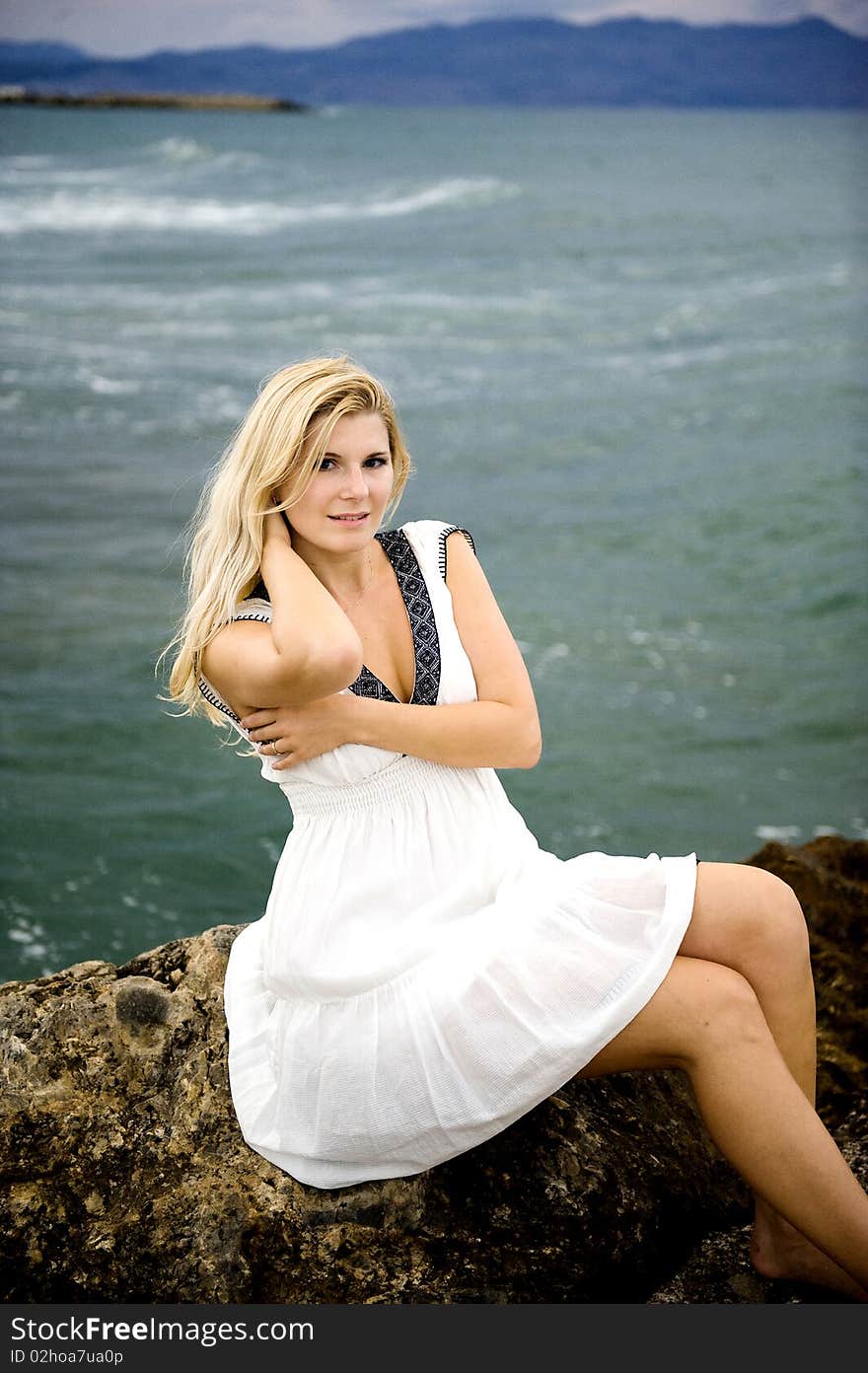 Young beautiful romantic woman in white dress dancing with shawl near blue sea