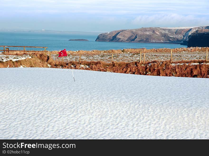 Snow covering on a golf course in ireland in winter with sea and cliffs in background. Snow covering on a golf course in ireland in winter with sea and cliffs in background